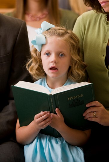 Young girl singing while holding an open hymnbook