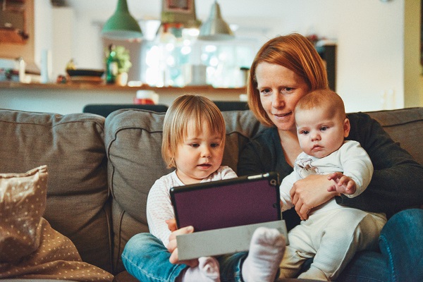 Mother sitting on couch with two small children, watching something on a tablet
