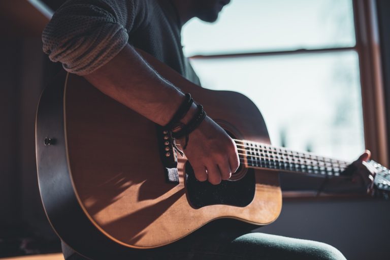 Man playing an acoustic guitar near a window